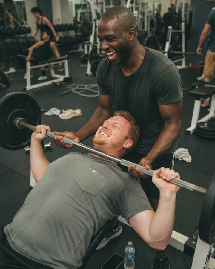 Two friends laughing mid bench press
